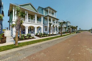 A row of two-story houses with balconies, a paved street, and palm trees. - Real Good Tan | Golf Views | Steps to Beach (Port Aransas)