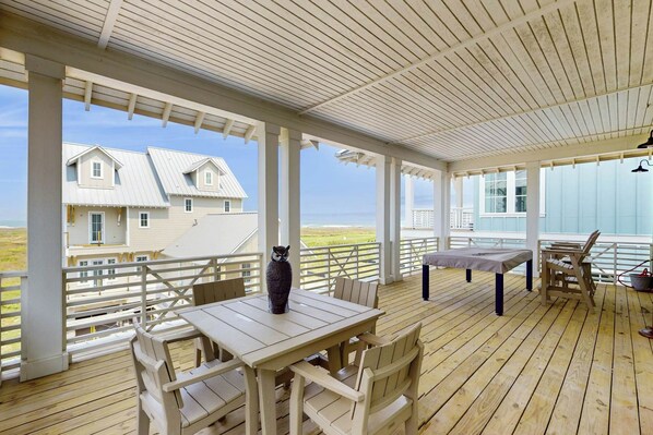 A covered outdoor area with a table and chairs, a view of a house, and a railing. - Real Good Tan | Golf Views | Steps to Beach (Port Aransas)