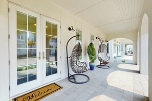 A covered walkway with a welcome mat, glass doors, and hanging chairs. - Real Good Tan | Golf Views | Steps to Beach (Port Aransas)