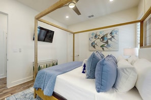 A bedroom with a four-poster bed, a flat-screen TV mounted on the wall, and a painting of birds. - Real Good Tan | Golf Views | Steps to Beach (Port Aransas)