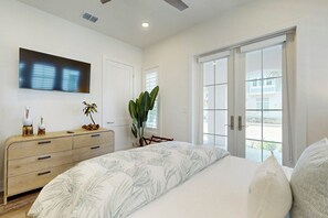 A bedroom with a large bed, a dresser, a television on the wall, and a large window with a view. - Real Good Tan | Golf Views | Steps to Beach (Port Aransas)