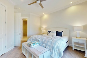 A bedroom with a bed, bedside tables, a bench, a ceiling fan, and a door leading to a bathroom. - Resort Views | Private Patio | Beach Escape (Port Aransas)
