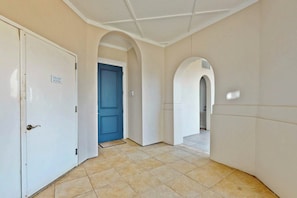 A hallway with a trash room door, a blue door, and a tiled floor. - Resort Views | Private Patio | Beach Escape (Port Aransas)