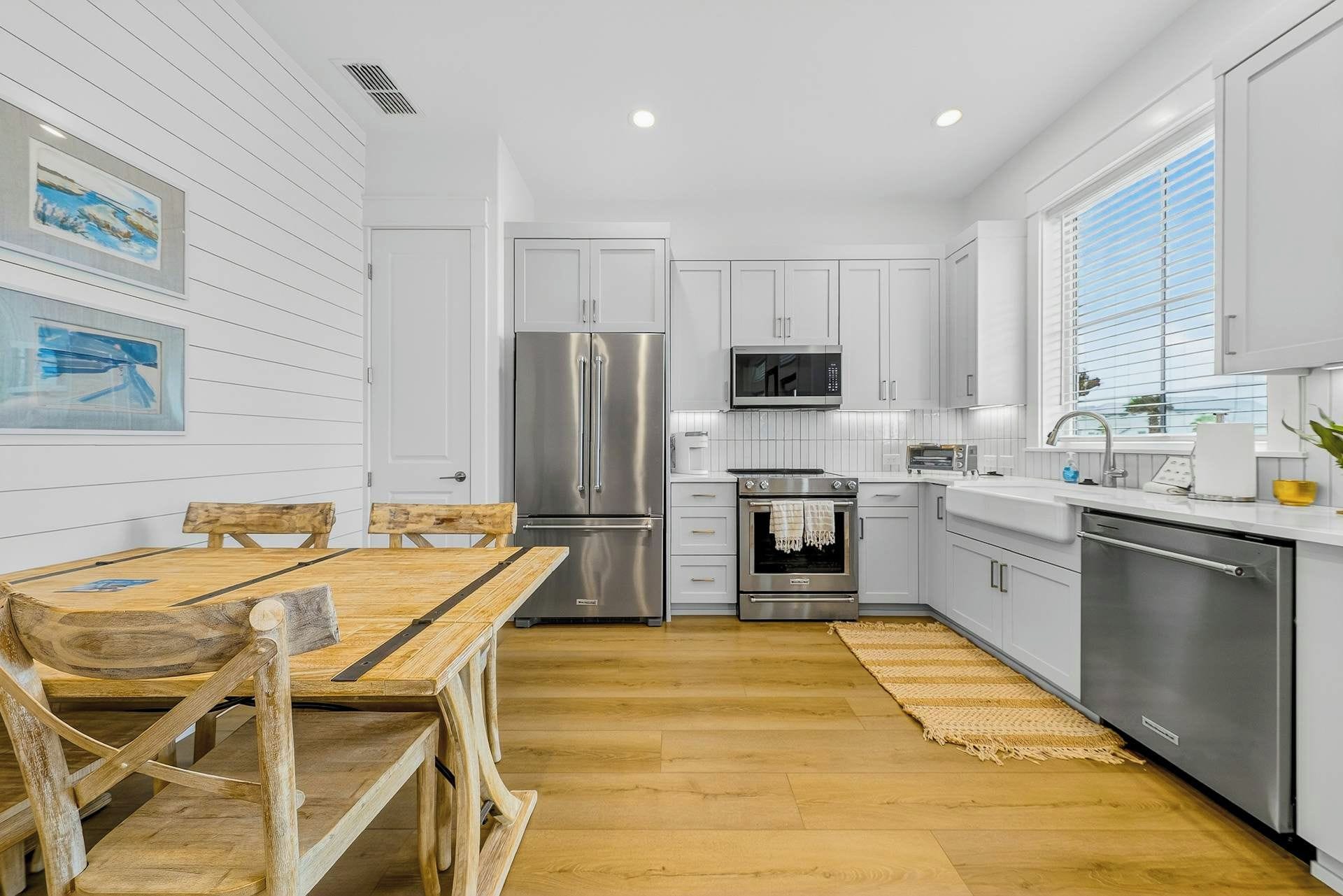 A modern kitchen with white cabinetry, stainless steel appliances, and a wooden dining table.