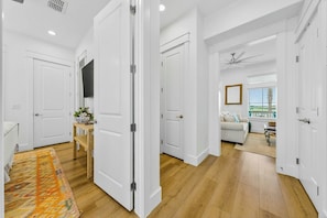 A hallway with white doors, a wooden floor, and a television on the wall. - Wave And Sea | Steps to Beach | Resort Amenities (Port Aransas)