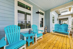 A covered porch with wooden flooring, turquoise Adirondack chairs, and a white door. - Wave And Sea | Steps to Beach | Resort Amenities (Port Aransas)