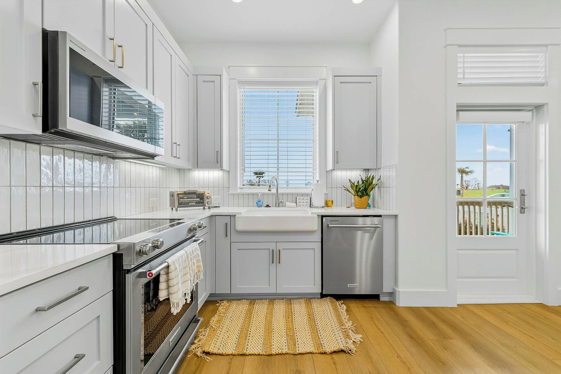 A modern kitchen with white cabinetry, a built-in oven, a dishwasher, and a window with blinds.