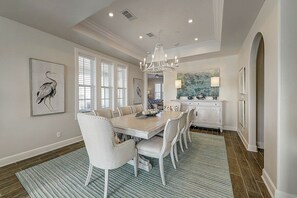 Een eetgedeelte met een lange tafel, witte stoelen en een kroonluchter.