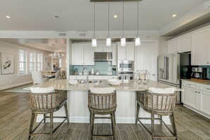 A spacious kitchen with a central island, bar stools, and modern appliances. - Palmilla Beach | Steps to Beach | Resort Amenities (Port Aransas)