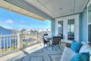 A balcony with a view of houses and a train track, furnished with a table, chairs, and a sofa. - Palmilla Beach | Steps to Beach | Resort Amenities (Port Aransas)