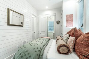 A bedroom with a bed, pillows, a mirror, and a window with blinds. - Ca-SEA-ta | Steps to Beach | Resort Amenities (Port Aransas)