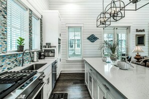 Een moderne keuken met een roestvrijstalen fornuis, witte kasten en een groot raam met zonwering.