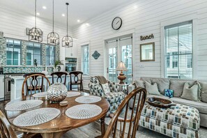 A dining area with a wooden table and chairs, a clock on the wall, and a bench with a view of the outside. - Ca-SEA-ta | Steps to Beach | Resort Amenities (Port Aransas)