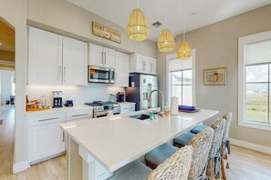 Een moderne keuken met witte kastjes, roestvrijstalen apparatuur, een groot eiland met zitplaatsen en hanglampen.
