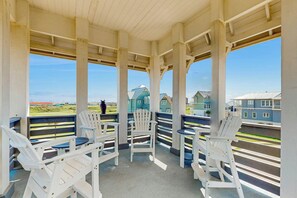 Een overdekt buitengebied met witte Adirondack-stoelen en uitzicht op huizen.