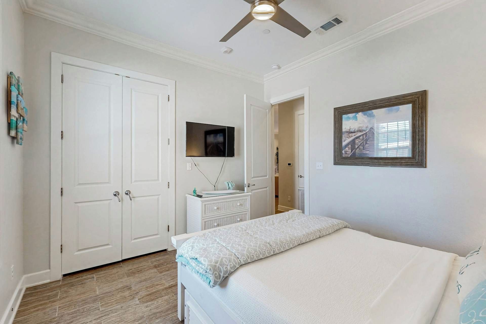 Une chambre à coucher avec un lit, un ventilateur de plafond, un téléviseur et un tableau accroché au mur.