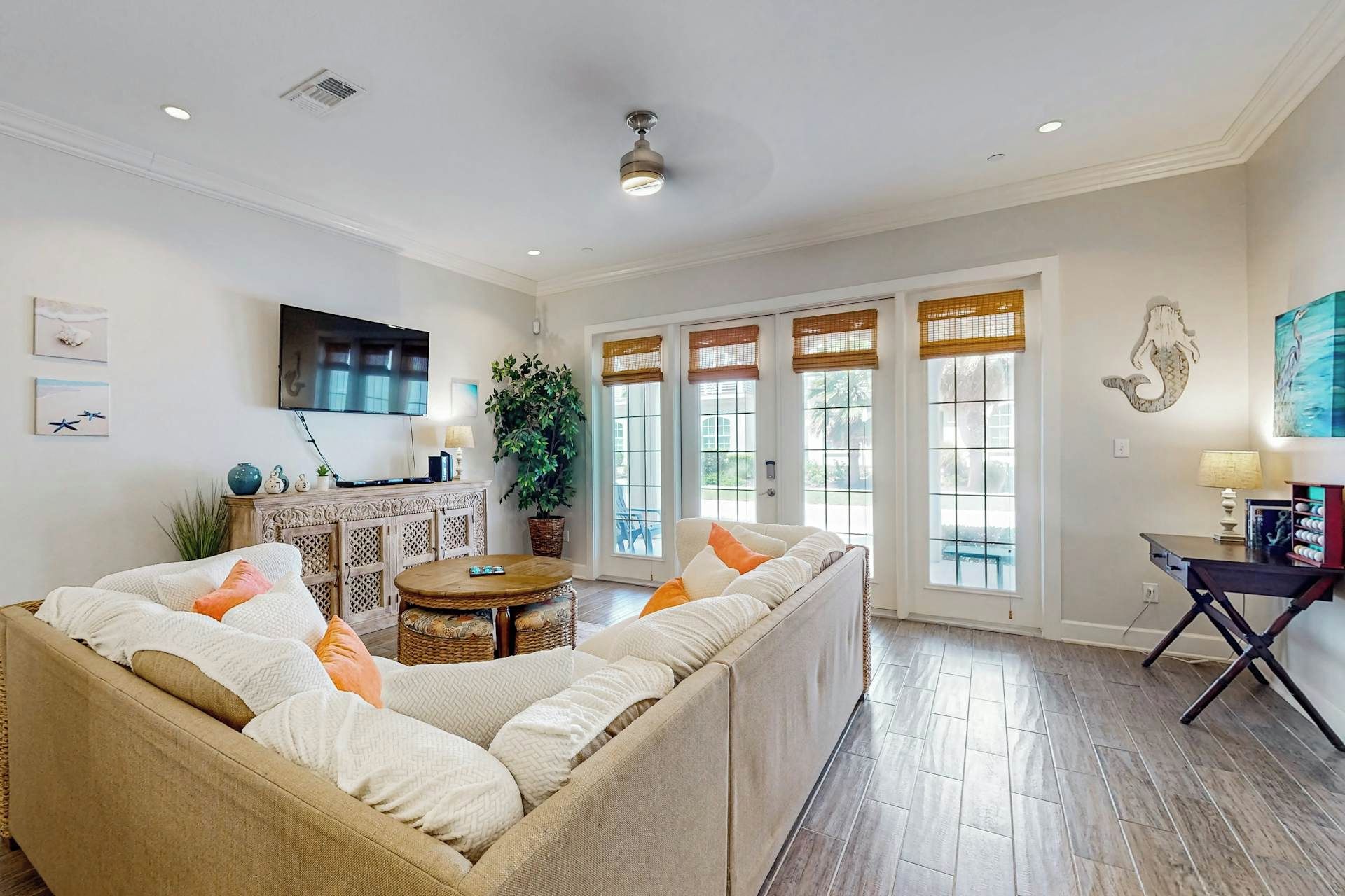 A living room with a large sectional sofa, a flat-screen TV, a dining area with a table and chairs, and a large window with blinds.