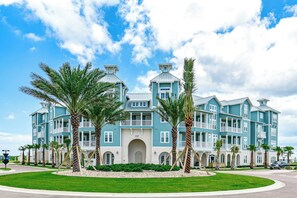 A large, multi-story hotel with a light blue exterior, multiple balconies, and palm trees in the foreground. - Coastal Getaway| Steps to Beach | Resort Amenities (Port Aransas)