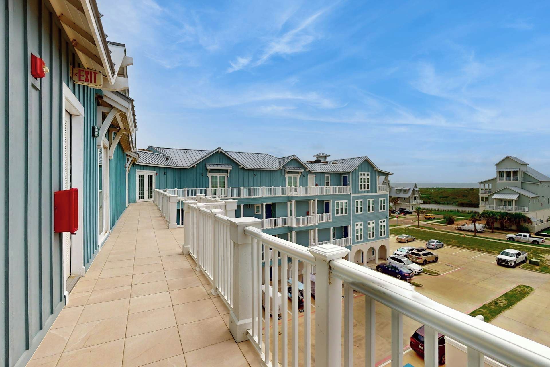 A balcony with a view of a coastal area, including a parking lot and buildings.