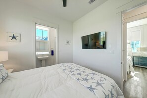 Une chambre à coucher avec un lit, un miroir, une télévision et une porte menant à la salle de bain.