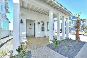 Ein Haus am Meer mit einer überdachten Veranda, weißen Säulen und einer Holzterrasse.