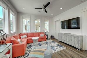 Ein Wohnzimmer mit einem Ecksofa, einem an der Wand befestigten Fernseher und einem Deckenventilator.