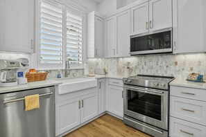 A modern kitchen with white cabinets, stainless steel appliances, and a microwave above the stove. - Starfish Cove | Steps to Beach | Resort Amenities (Port Aransas)