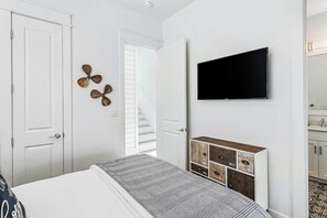 A bedroom with a bed, a TV mounted on the wall, a chest of drawers, and a door. - Sunrise At Anchor | Water Views | Steps to Beach (Port Aransas)