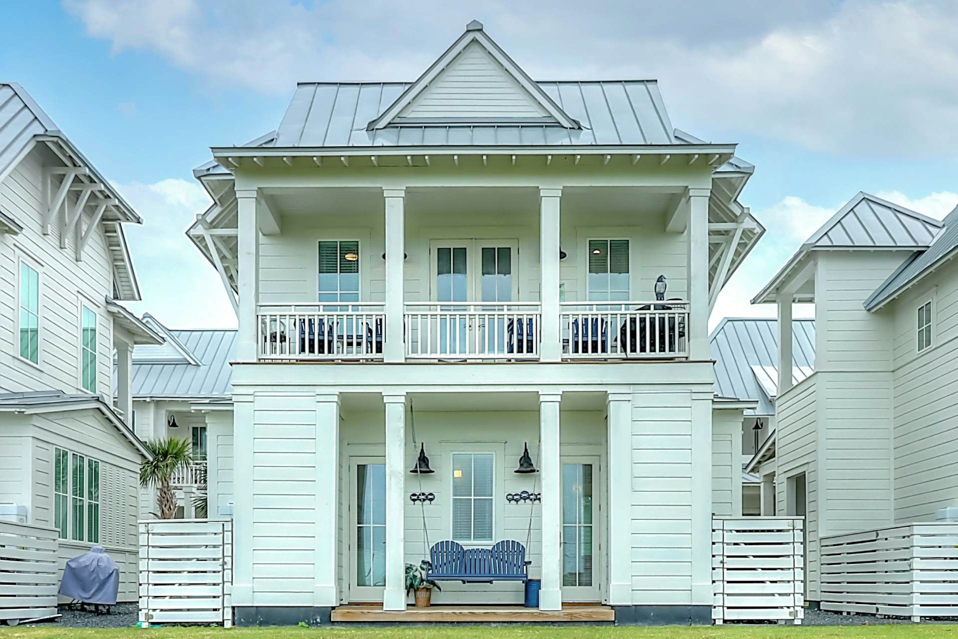 Une maison à deux étages avec un balcon, une véranda à l’avant avec un banc et une porte de garage.