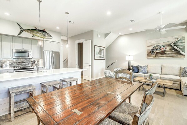 A modern kitchen with a central island, stainless steel appliances, and a dining area with a wooden table and chairs. - Top Of The Shoreline | Golf Views | Steps to Beach (Port Aransas)