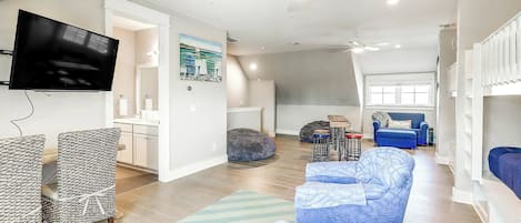 A spacious living area with a flat-screen TV, seating, a ceiling fan, and a large window.
