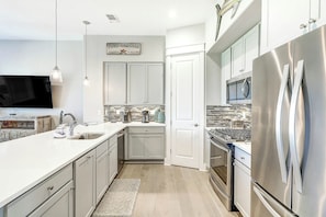 A modern kitchen with stainless steel appliances, a flat-screen TV, and a white backsplash. - Top Of The Shoreline | Golf Views | Steps to Beach (Port Aransas)