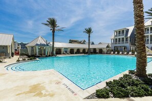 A swimming pool with a clear blue water, surrounded by palm trees and a building with a white facade. - Vida Del Mar | Steps to Beach | Resort Amenities (Port Aransas)