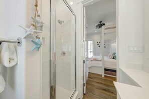 A modern bathroom with a glass shower enclosure, white tiled walls, and a visible towel rack. - Vida Del Mar | Steps to Beach | Resort Amenities (Port Aransas)