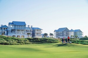 A golf course with a clubhouse and large houses in the background. - Vida Del Mar | Steps to Beach | Resort Amenities (Port Aransas)