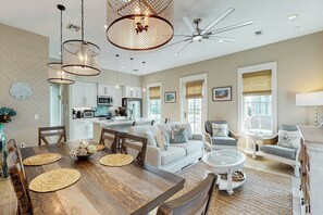 A spacious living area with a dining table, sofas, and a kitchen in the background. - We Be Beachin' | Golf Views | Pet Friendly (Port Aransas)