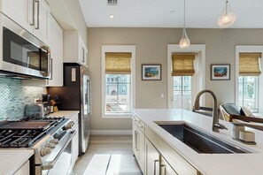 A modern kitchen with a gas stove, oven, microwave, and a large island with a sink. - We Be Beachin' | Golf Views | Pet Friendly (Port Aransas)