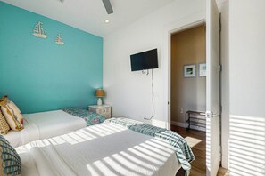 A bedroom with a bed, a nightstand, a TV mounted on the wall, and a door leading to another room. - We Be Beachin' | Golf Views | Pet Friendly (Port Aransas)
