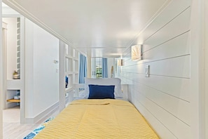 Ein schmaler Flur führt zu einem Schlafzimmer mit einem Bett, einem eingebauten Kleiderschrank und Blick durch eine Glastür.
