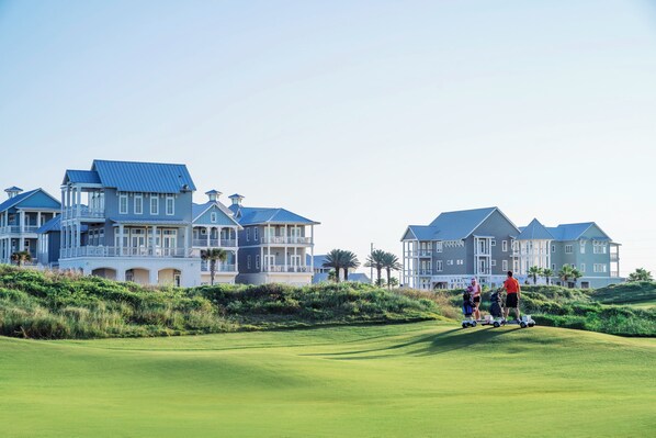 A golf course with a clubhouse and large houses in the background. - Palmilla Beach Escape | Steps to Beach (Port Aransas)