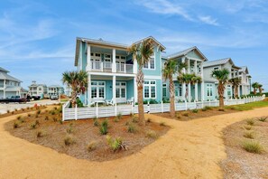 A two-story beachfront house with a balcony, surrounded by a white fence and palm trees. - Palmilla Beach Escape | Steps to Beach (Port Aransas)
