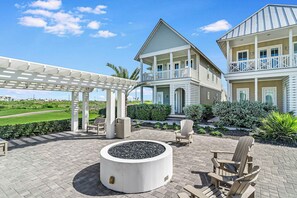 Ein zweigeschossiges Haus mit einer überdachten Terrasse, Sitzgelegenheiten im Freien und einem Feuerkorb.