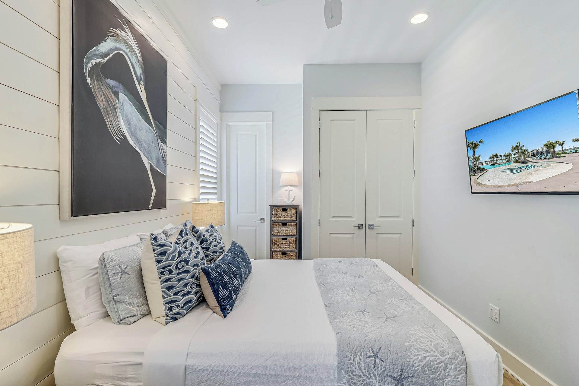 A bedroom with a bed, a large painting, a television, and a door.