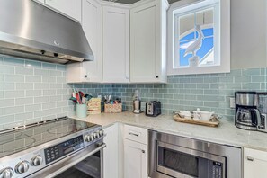 A modern kitchen with white cabinets, a stainless steel range, an oven, a microwave, and a window with a decorative bird. - Family Beach Retreat| Bunk Room | Resort Amenities (Port Aransas)