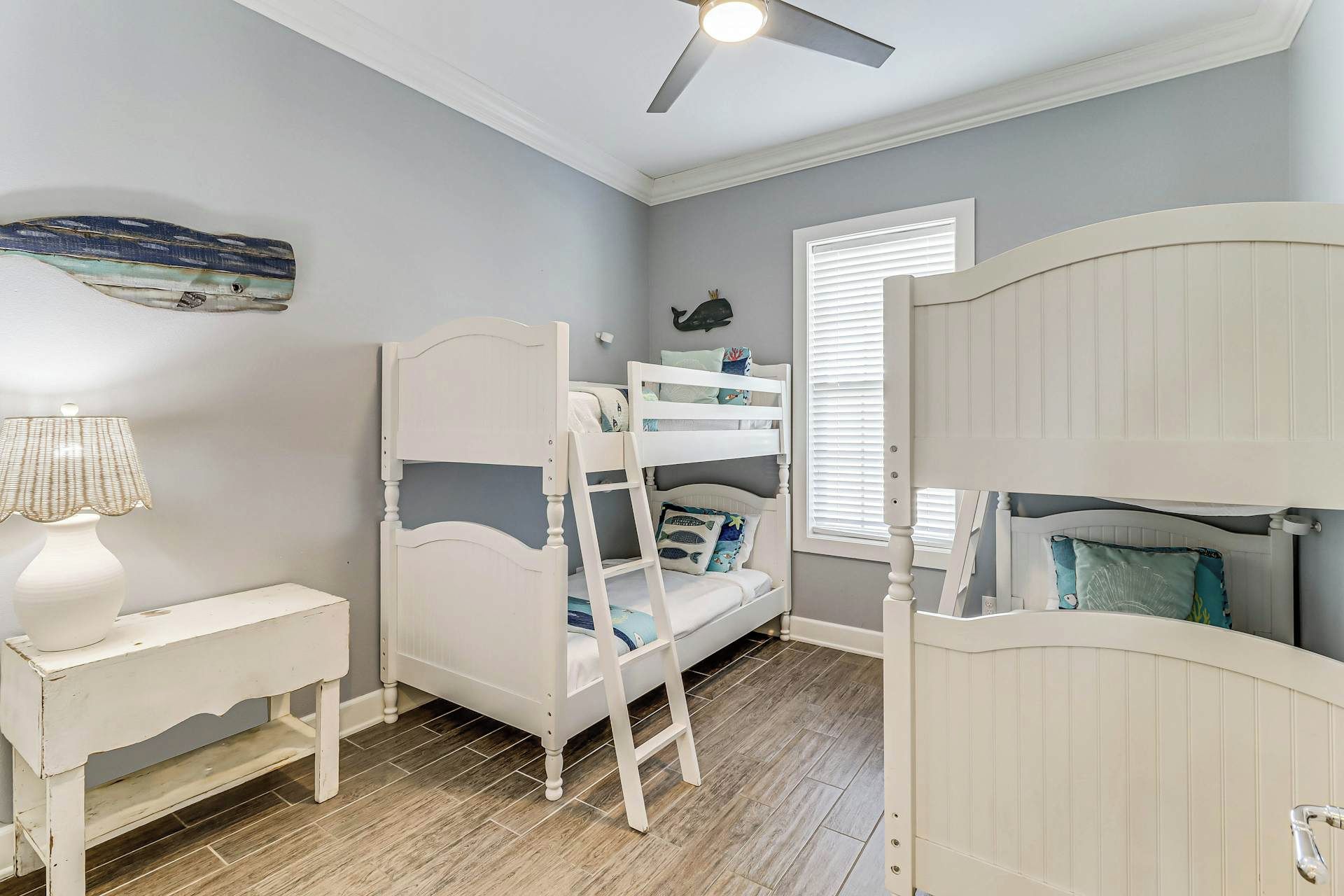 Ein Kinderstockbett mit einer Leiter, ein Nachttisch mit Lampe sowie ein Fenster mit Jalousien.