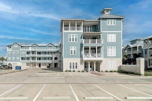 A multi-story residential building with balconies, a parking lot in front, and a clear sky. - Family Beach Retreat| Bunk Room | Resort Amenities (Port Aransas)