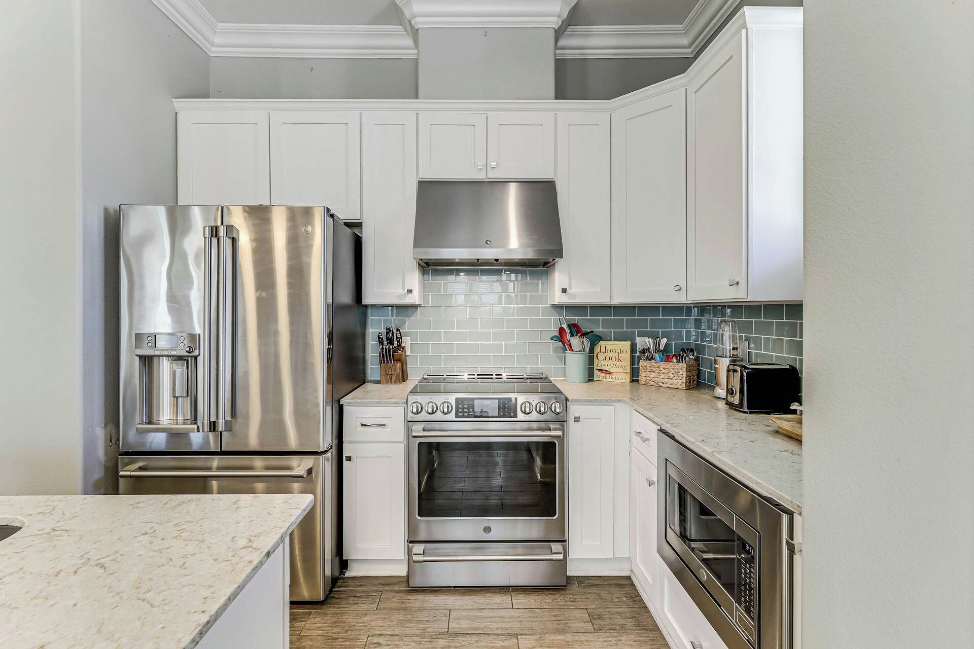 Una cocina moderna con electrodomésticos de acero inoxidable, armarios blancos y salpicadero de azulejos.