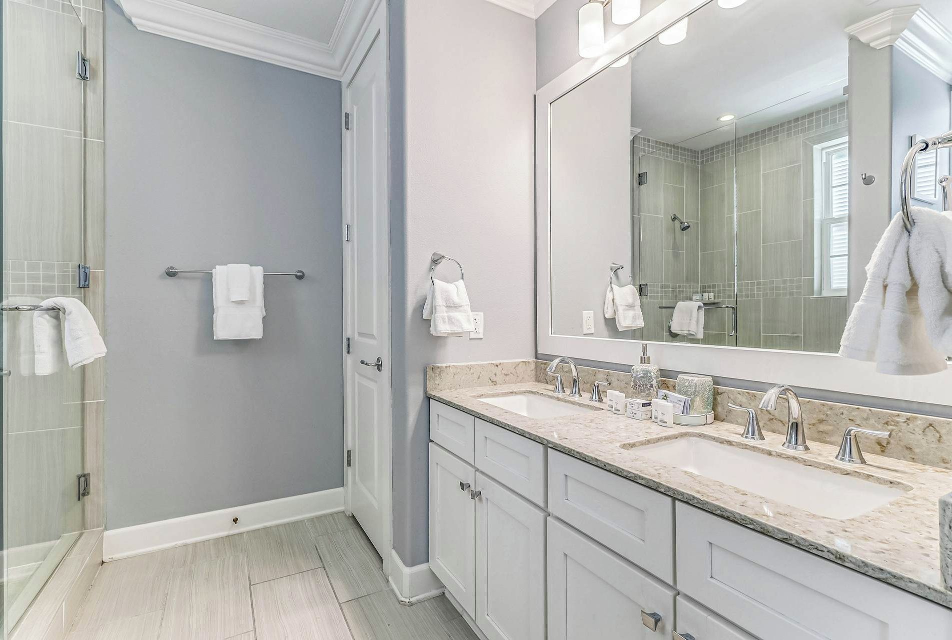 Step into your serene en-suite bathroom featuring a spacious walk-in shower with elegant tile work, dual vanities with granite counters, and plush towels ready for your arrival—everything you need to unwind after a day of exploration.