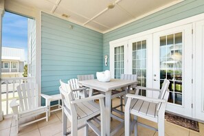 Eine überdachte Terrasse mit einem weißen Tisch und Stühlen, eine weiße Tür mit Glasfeldern und ein Blick auf ein Haus im Hintergrund.