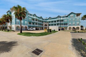 A multi-story hotel with a central courtyard, outdoor parking, and a pool area. - Gulf Views | Chef’s Kitchen | Beach Escape (Port Aransas)